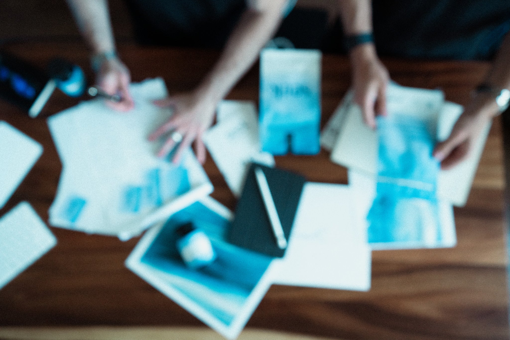 Blurred image of hands working on a creative project at Seek® Coffee's workspace, with scattered brand materials, packaging designs, and a notebook on the table. The scene captures the collaborative and thoughtful process behind developing Seek®’s wellness-focused coffee brand.