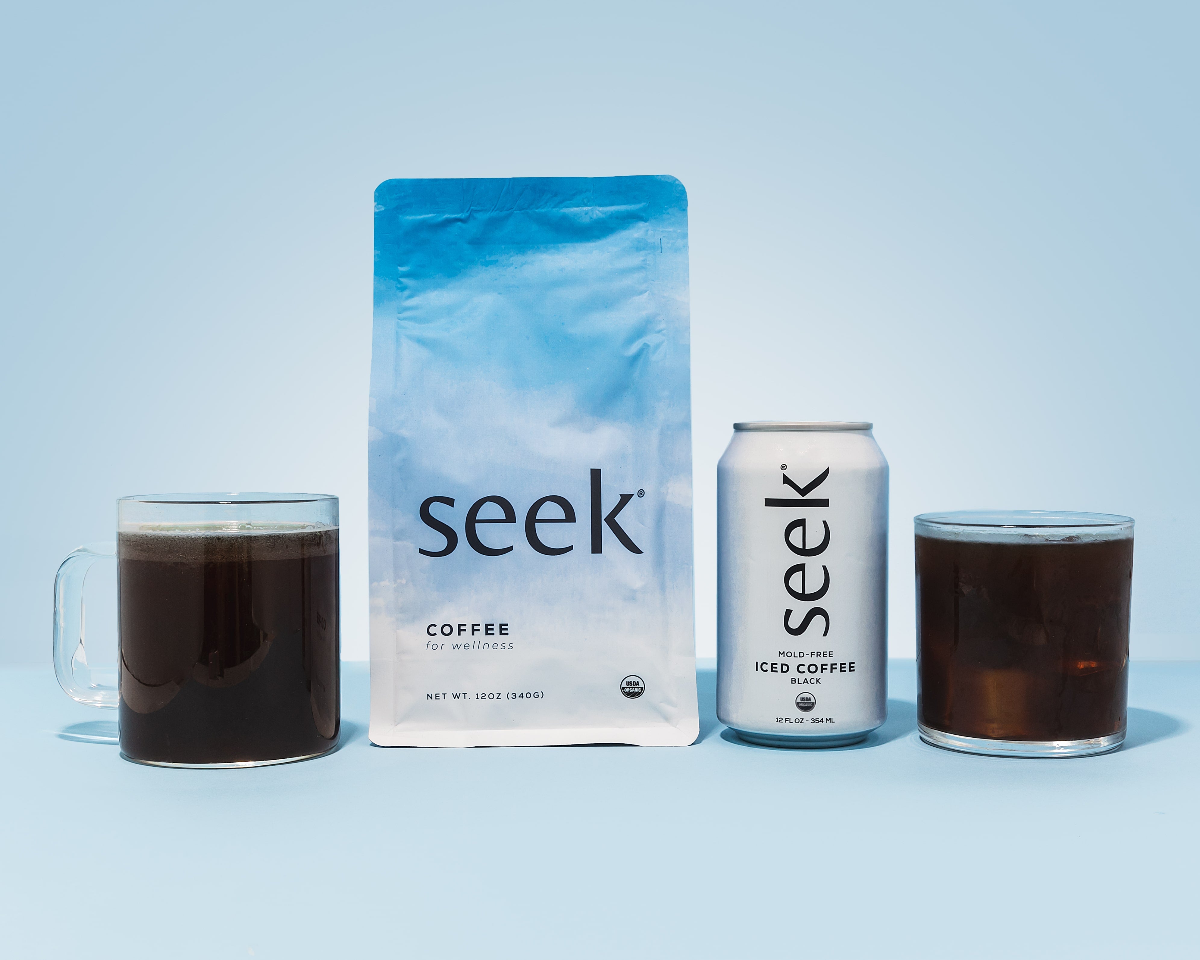 Seek® Coffee hero image featuring a bag of organic coffee, a can of mold-free iced coffee, and two glass mugs filled with rich, black coffee. Displayed on a light blue background, this setup highlights Seek®’s commitment to wellness-focused, clean, and low-acid coffee options designed for those seeking a health-conscious coffee experience.