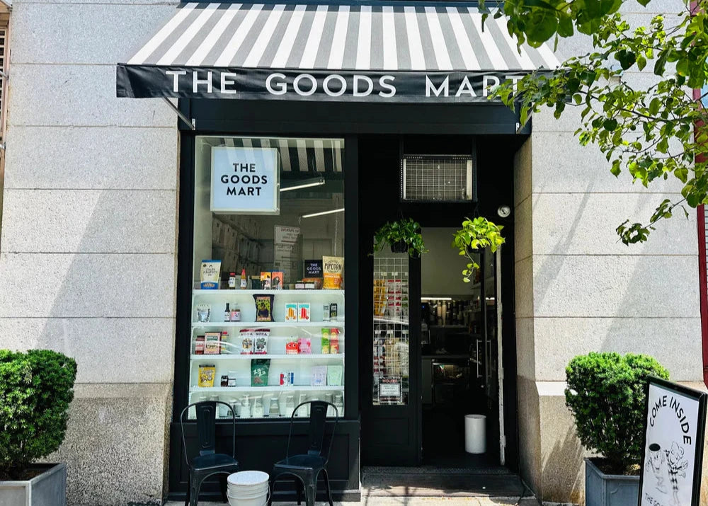 Storefront of 'The Goods Mart' with striped awning and glass door.