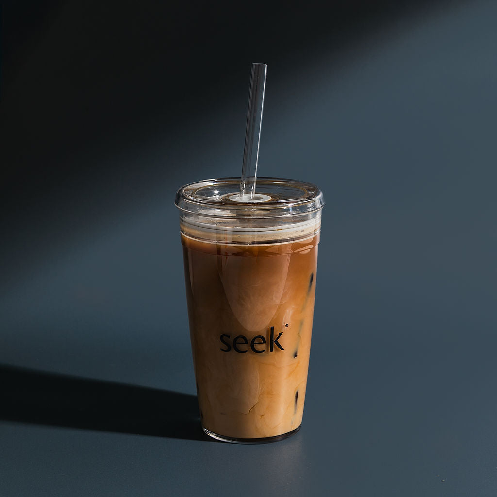 Iced coffee in a clear cup with a straw on a dark background, featuring the brand 'seek'.