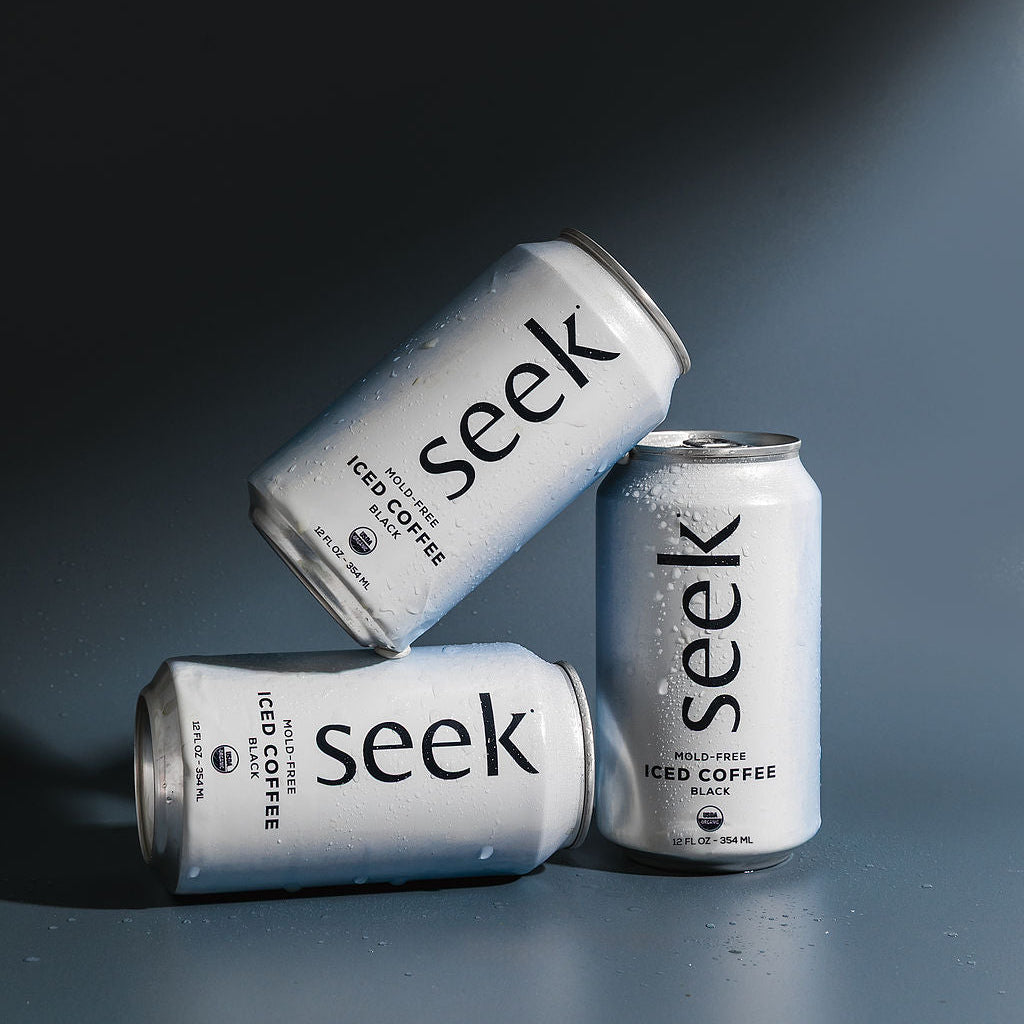 Three cans of 'seek' iced coffee on a reflective surface with a dark background