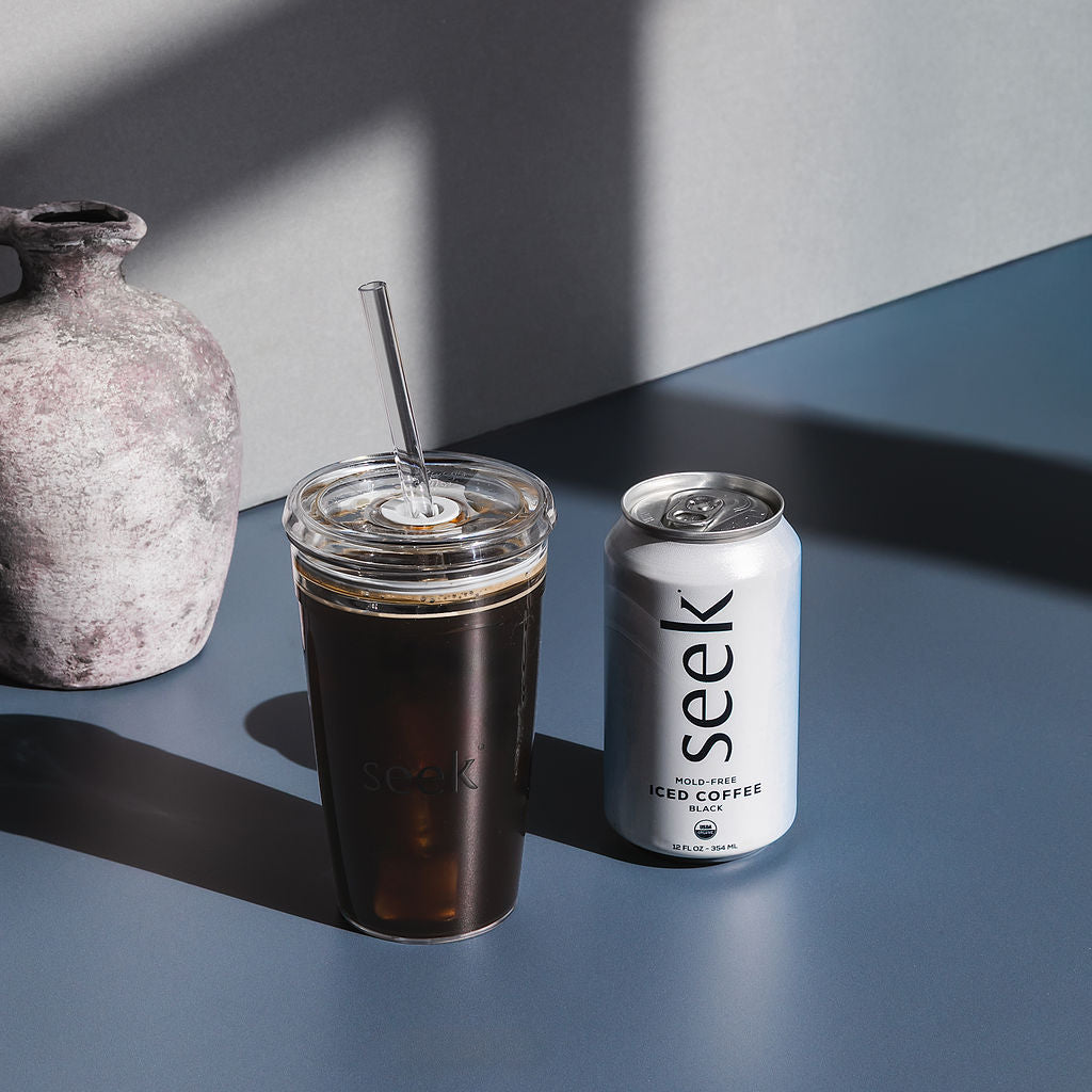 Iced coffee in a clear cup with a straw and a can of 'seek' iced coffee on a dark surface.