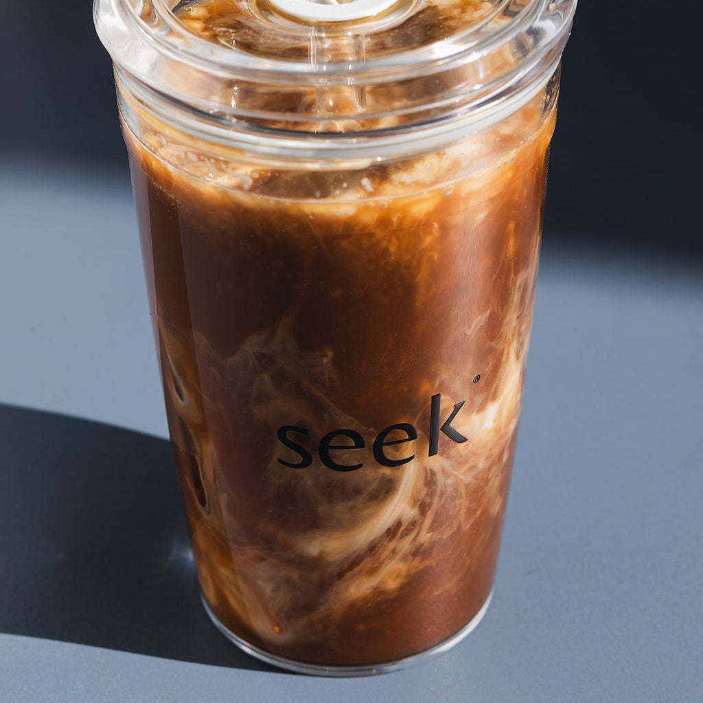 Clear cup with iced coffee and 'seek' branding on a dark background