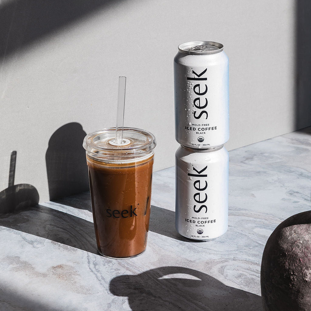 Two cans and a glass of iced coffee with 'seek' branding on a marble surface.