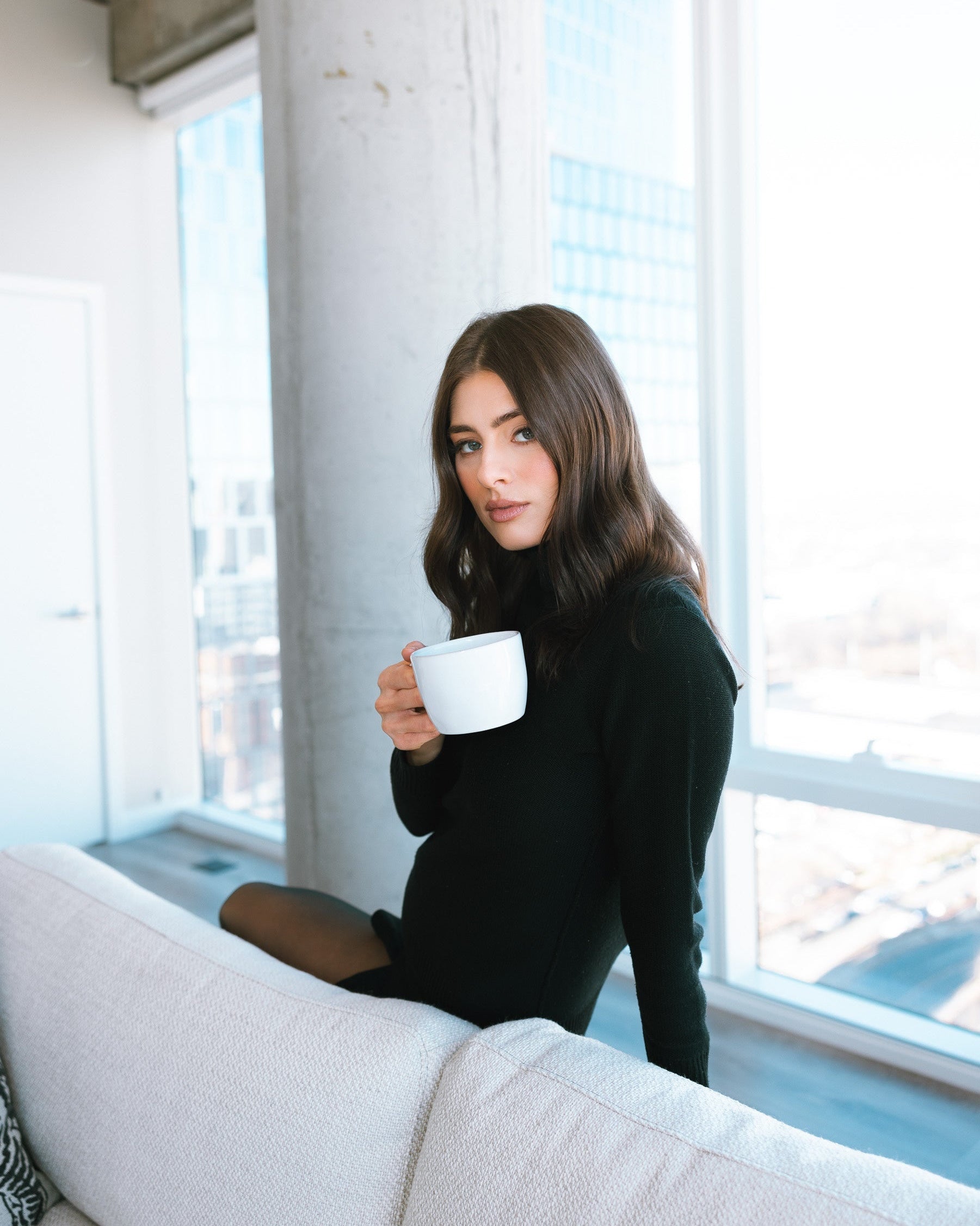 Woman holding a white mug in a room with large windows