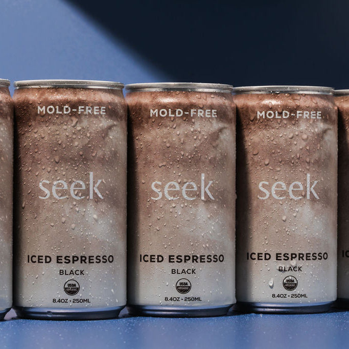Five cans of Seek Iced Espresso Black beverage lined up on a blue surface against a blue background.