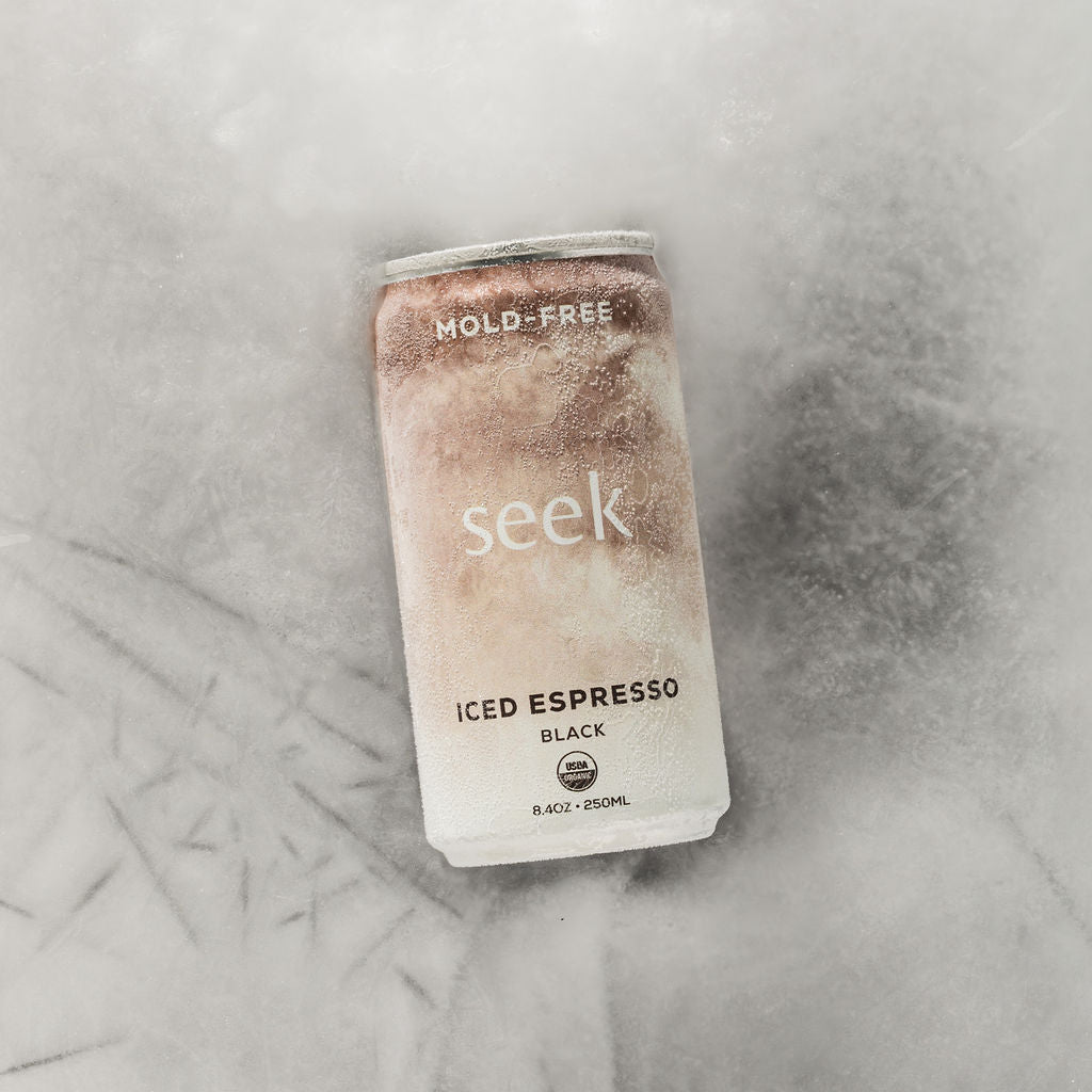 A single can of Seek Iced Espresso Black coffee, heavily frosted with ice, lying on a textured light gray surface.