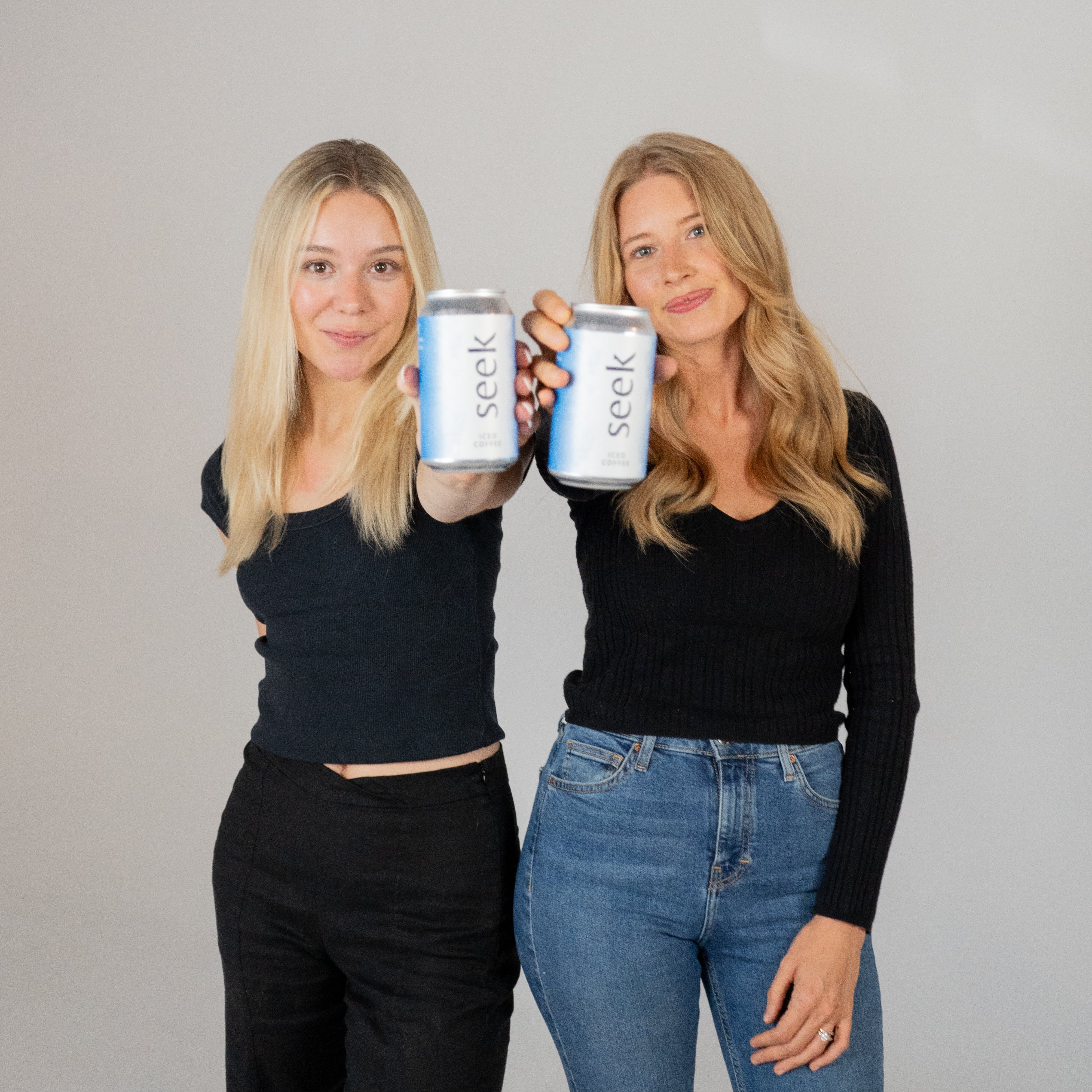 Two young beautiful women holding cans of seek® ice coffee laughing and smiling because of the community there are part of through seek®